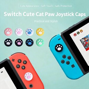 Puede incluir: Un conjunto de tapas de joystick con forma de pata de gato para consola Switch. Las tapas son de varios colores, incluyendo rosa, blanco, azul y amarillo, y tienen un dise&ntilde;o de huella de pata. La imagen tambi&eacute;n muestra un mando Switch rojo y azul.