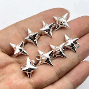 Peut inclure: Collection de breloques en métal argenté en forme d'étoile. Chaque breloque comporte plusieurs pointes et une petite boucle pour l'attacher à des bijoux ou autres créations. Les breloques sont présentées sur un fond neutre.