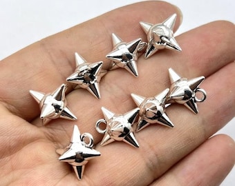 May include: A collection of seven silver-toned metal star-shaped charms, each featuring four pointed rays and a central conical protrusion. Several of these charms include a small circular jump ring attached to one of the points for hanging purposes.