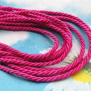 May include: A close-up of a spool of bright pink twisted cord. The cord is made of a soft, silky material and has a subtle sheen.