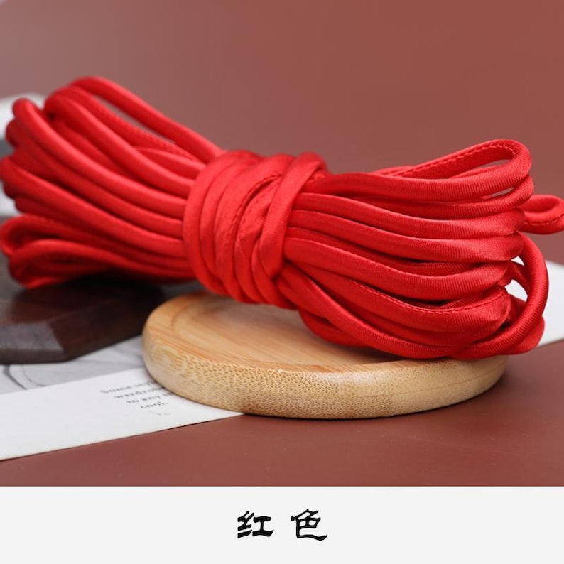 May include: A spool of bright red satin cord, wound neatly on a wooden surface. The text "红色" is visible below the cord.