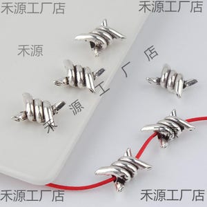 Peut inclure: Cinq breloques en fil de fer barbelé argentées, chacune avec un angle différent, sont présentées sur une surface blanche. Deux des breloques sont sur une ficelle rouge. Le texte "禾源工厂店" apparaît sur l'image.