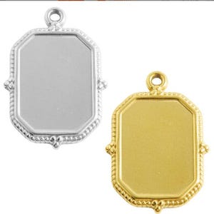 Puede incluir: Dos colgantes rectangulares, uno plateado y otro dorado. Cada uno tiene un marco octogonal con un borde decorativo en forma de cuerda y pequeños detalles decorativos en las esquinas. Un pequeño lazo en la parte superior para una cadena.