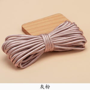 May include: A tightly wound bundle of dusty rose satin cord, secured with a matching wrap. The cord is displayed on a small, light-coloured wooden block. The Chinese characters "gray powder" are at the bottom.
