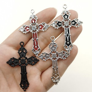 May include: Three silver-tone metal cross charms with ornate designs. One cross is red, one is black, and one is silver.