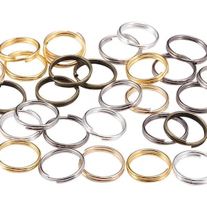 Op de afbeelding: Een verzameling van verschillende metalen sleutelringen in goud, zilver en brons. De sleutelringen zijn allemaal rond en hebben een gladde afwerking.