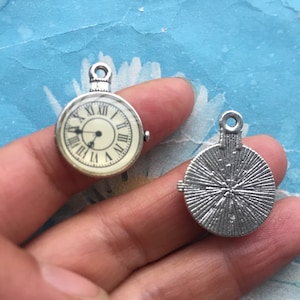 May include: Two silver-toned metal charms, one with a round clock face and the other with a sunburst design.