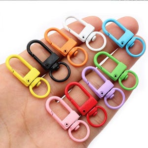 Può includere: Una collezione di chiusure girevoli in metallo colorato in varie tonalità, tra cui giallo, nero, arancione, bianco, blu, verde, viola, rosso e rosa. Ogni chiusura ha un anello di attacco. Ideali per portachiavi, cordini e progetti artigianali.