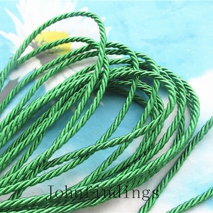 Puede incluir: Primer plano de una bobina de cordón verde trenzado. El cordón está hecho de un material suave y sedoso y tiene un brillo sutil.