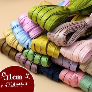 Può includere: Una collezione di nastri di raso colorati in varie tonalità, tra cui verde, rosa, blu e oro. I nastri sono larghi circa 1 cm e sono ordinatamente arrotolati, mostrando la loro consistenza liscia e i colori vivaci. Ideali per lavori di artigianato e progetti decorativi.