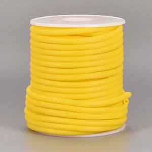 Può includere: Un rotolo di cordoncino elastico giallo brillante. Il cordoncino è avvolto strettamente attorno a un rotolo di plastica bianca.