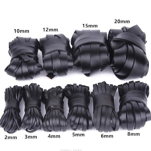 Puede incluir: Diez bobinas de cordón de cuero negro dispuestas en dos filas. La fila superior presenta anchos de 10mm, 12mm, 15mm y 20mm. La fila inferior muestra anchos de 2mm, 3mm, 4mm, 5mm, 6mm y 8mm. Cada bobina está etiquetada con su medida de ancho.