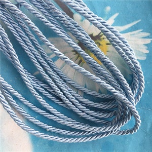 May include: A close-up of a bundle of light blue twisted cord. The cord is made of a soft, silky material and has a subtle sheen.