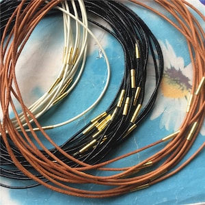 Puede incluir: Una colección de cordones de cuero con detalles metálicos dorados. Los cordones son de tres colores: marrón, negro y blanco.