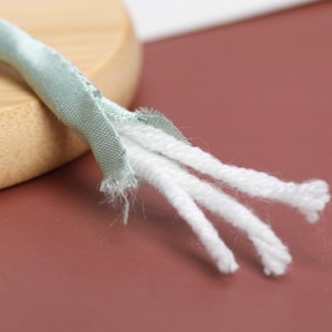 May include: Close-up of a light green fabric cord with three white cotton cords coming out of the end.