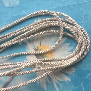 May include: A close-up of a silver braided cord, showing the texture and detail of the cord. The cord is lying on a blue and white patterned surface.