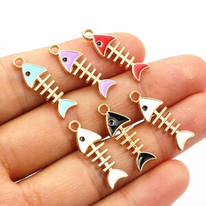 May include: Six colorful fish bone charms with gold-tone metal frames. Each charm features a different color: red, purple, black, white, and blue. The charms are small and have a loop at the top for attaching to jewelry.