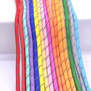 May include: A collection of colorful cords in various shades, including red, purple, yellow, and orange. Each cord has a textured pattern with a thin, darker stripe running along its length. The cords are arranged closely together, creating a vibrant display.