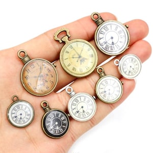 May include: A collection of antique-style pocket watch charms in various sizes and finishes. The charms feature Roman numeral clock faces in bronze, silver, and black tones. Some have clear glass covers, while others have open faces.