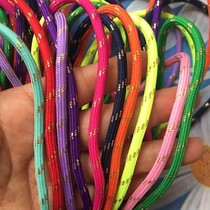 May include: A selection of brightly coloured cords in shades like red, pink, and green, each featuring small gold flecks. The cords are held in a hand, highlighting their vibrant colours and textures. Metric measurements apply.