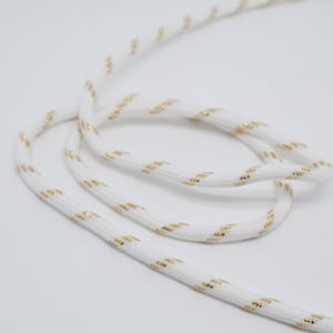 May include: White rope with gold metallic accents. The rope is tightly woven and has a subtle sheen. The gold accents are evenly spaced along the length of the rope, creating a decorative pattern. This rope is suitable for various craft projects.