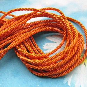 Peut inclure: Une bobine de cordon torsadé orange vif. Le cordon est fait d'un matériau doux et soyeux, idéal pour les projets d'artisanat.