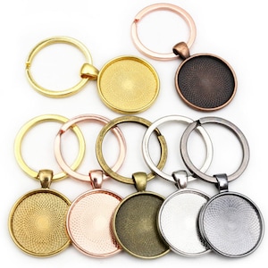 May include: Assortment of eight keychains with round, metal, blank, circular, glass-like, picture frames. The keychains are in various colors, including gold, silver, rose gold, and bronze.