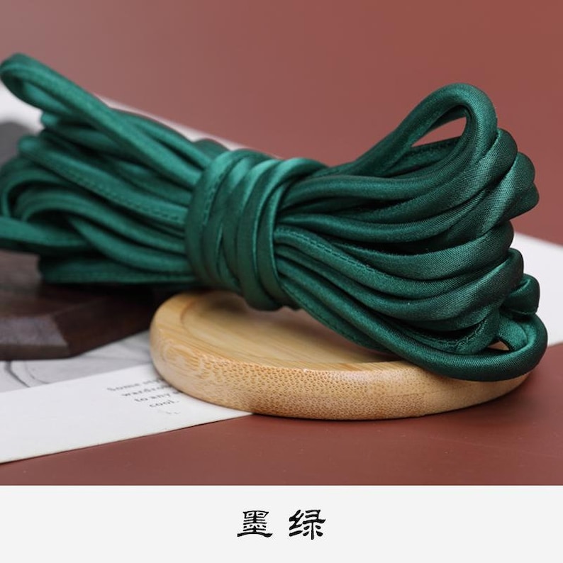 May include: A spool of dark green satin ribbon, coiled on a wooden surface. The ribbon is smooth and shiny.