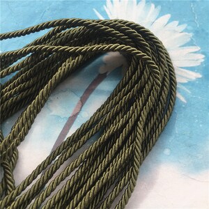 May include: A close-up of a spool of dark green twisted cord. The cord is made of a soft, woven fabric and has a subtle sheen.