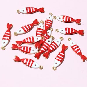 May include: A selection of red and white fish-shaped charms with gold-coloured loops for jewellery making. The charms feature a red tail and stripes on a white body. These charms are suitable for creating earrings, necklaces, or bracelets.