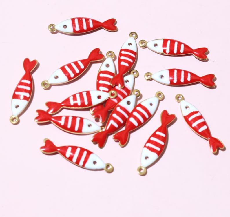 May include: A selection of red and white fish-shaped charms with gold-coloured loops for jewellery making. The charms feature a red tail and stripes on a white body. These charms are suitable for creating earrings, necklaces, or bracelets.