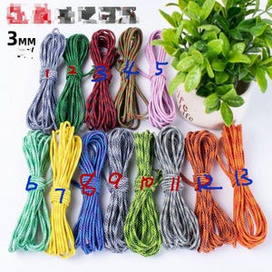 Puede incluir: Una colección de cordones coloridos de 3 mm de diámetro en varios tonos, incluyendo azul, verde, rojo y naranja. Los cordones están agrupados y atados, con una planta en una maceta blanca en el fondo. La imagen está bien iluminada.