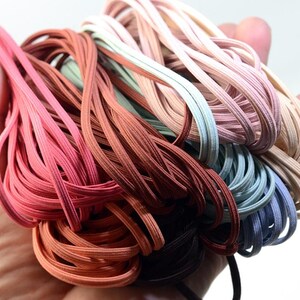 May include: A collection of colorful elastic bands in various shades of pink, brown, and blue. The bands are tightly bundled together, showcasing a range of colors from light pastels to deeper, richer tones. The elastic appears to be smooth and flexible.