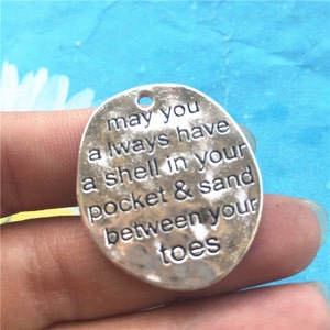 May include: Silver charm with the text "may you always have a shell in your pocket & sand between your toes".