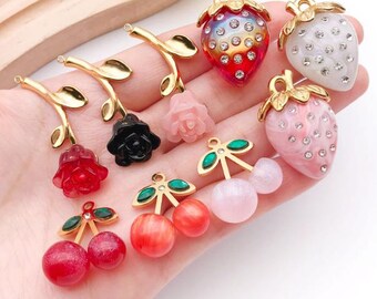 May include: A collection of colorful, decorative charms featuring various fruit and floral designs. The charms include strawberries, cherries, and roses in red, pink, and white, with gold-colored accents and sparkling embellishments.
