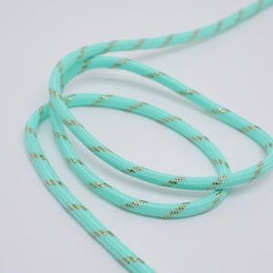 May include: Close-up of a length of turquoise rope with gold flecks. The rope is coiled and has a textured surface. The background is plain white.