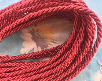 May include: A close-up of a spool of red twisted cord. The cord is made of a soft, silky material and has a subtle sheen.
