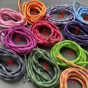 Puede incluir: Una colección de cuerdas enrolladas en varios colores, incluyendo rosa, naranja, morado, azul y verde. Cada cuerda está numerada, mostrando una gama de tonos y patrones. Las cuerdas parecen estar hechas de un material tejido duradero.