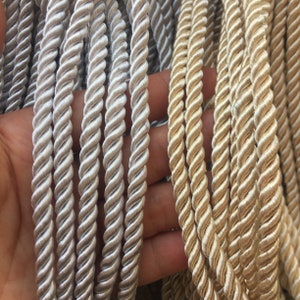 Könnte beinhalten: Zwei Arten von gedrehtem Kordelband, eines silberfarben und eines goldfarben. Die Kordel ist aus einem weichen, seidenartigen Material.