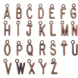 May include: A set of 26 antique gold-toned metal alphabet letter charms with a loop at the top for hanging. The letters are arranged in alphabetical order.