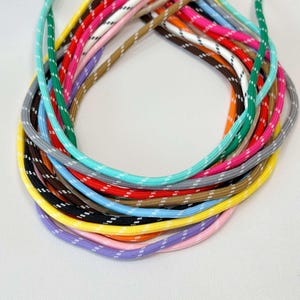 Może przedstawiać: Kolekcja kolorowych sznurków, każdy w unikalnym kolorze i z białym wzorem w kropki. Sznurki ułożone są w okrąg, prezentując różnorodne odcienie, w tym zielony, różowy, żółty i niebieski. Sznurki wydają się być wykonane z trwałego, tkanego materiału.