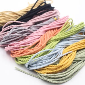 Op de afbeelding: Een verzameling kleurrijke touwen in verschillende tinten, waaronder zwart, roze, oranje, groen, blauw en geel. De touwen zijn strak opgerold en lijken gemaakt te zijn van een zacht, flexibel materiaal. De afbeelding is goed belicht en toont de levendige kleuren en texturen van het touw.