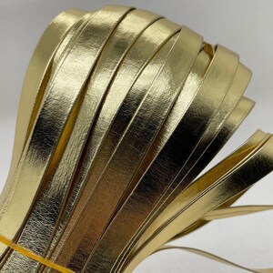 Könnte beinhalten: Nahaufnahme eines Bündels goldfarbenem Lederkordels. Das Kordel ist flach und hat eine glatte, glänzende Oberfläche.