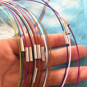 Op de afbeelding: Een set van 12 kleurrijke, dunne metalen kettingen met zilveren eindkappen. De kettingen zijn in een waaier vorm gerangschikt en worden in een hand gehouden.