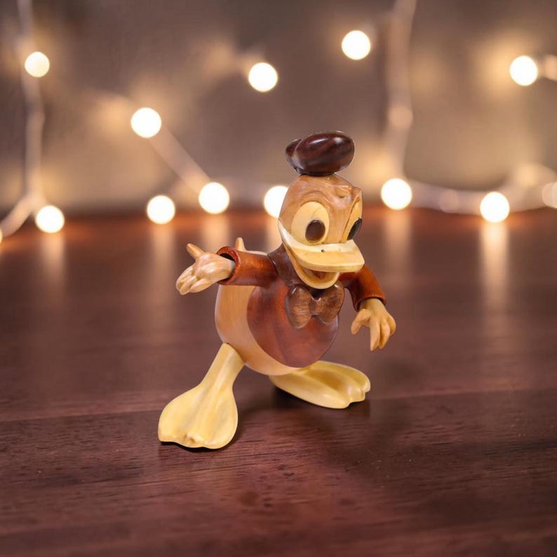 May include: Wooden Donald Duck figurine in a dynamic pose. The figure features a brown hat, jacket, and bow tie, with a light-colored beak, feet, and face. The background includes a string of soft, glowing lights, creating a warm ambiance.