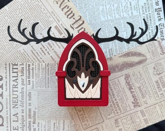 Può includere: Un ornamento in legno a strati rosso, crema e marrone scuro a forma di radio ad arco con corna di cervo nere che si estendono dai lati. L'area centrale dell'altoparlante presenta un design color crema a forma di fiamma.