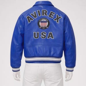 May include: A vibrant blue leather jacket with the word "AVIREX" arched across the back, above a circular emblem and the word "USA". The jacket has white stripes on the cuffs and hem.
