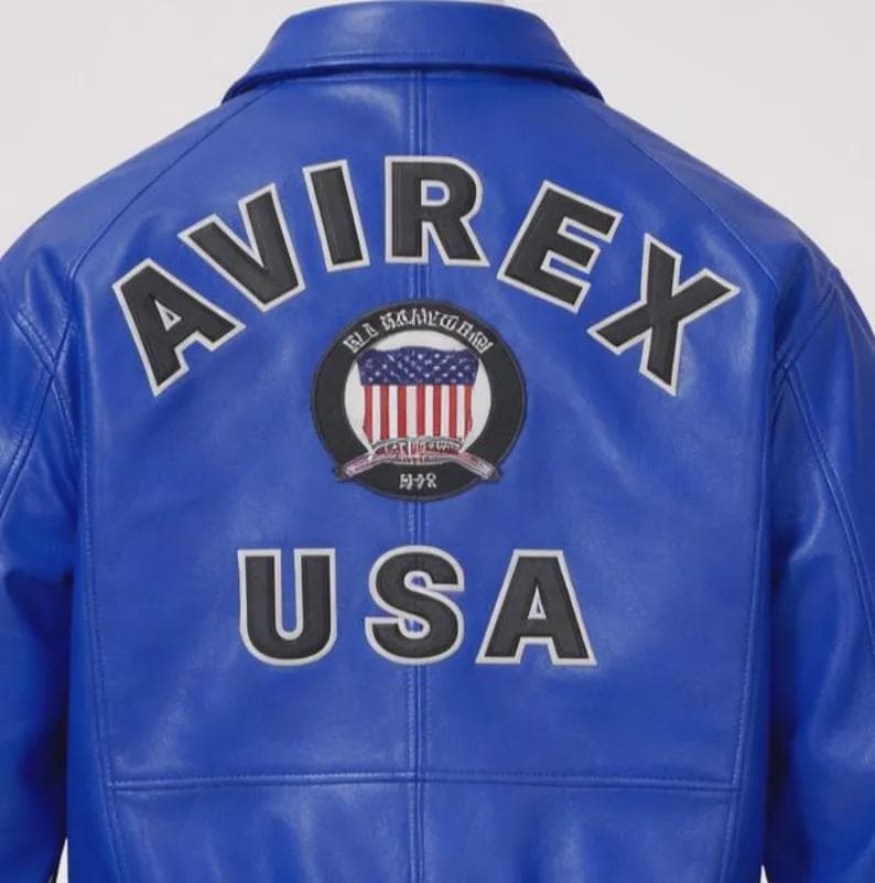 May include: A royal blue leather jacket with the word "AVIREX" arched across the top in white letters with a black outline. Below the word "AVIREX" is a circular patch with the American flag and the word "USA" in white letters with a black outline.