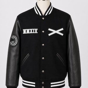 May include: A black varsity jacket with black leather sleeves and a snap-button front. The chest features white embroidered patches reading MMXIV and an X. The collar, cuffs, and hem have white stripes. A circular patch is on the right sleeve.