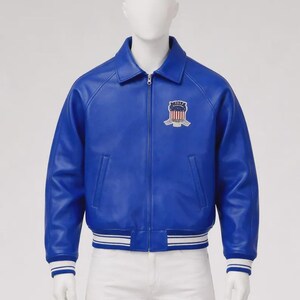 May include: A vibrant blue leather jacket with a zip-up front, a collared neckline, and a white and blue striped hem and cuffs. The jacket features a crest patch on the chest. The jacket is displayed on a mannequin.